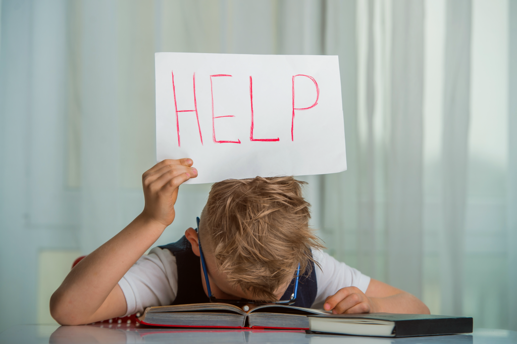 young boy with head in books holding help sign