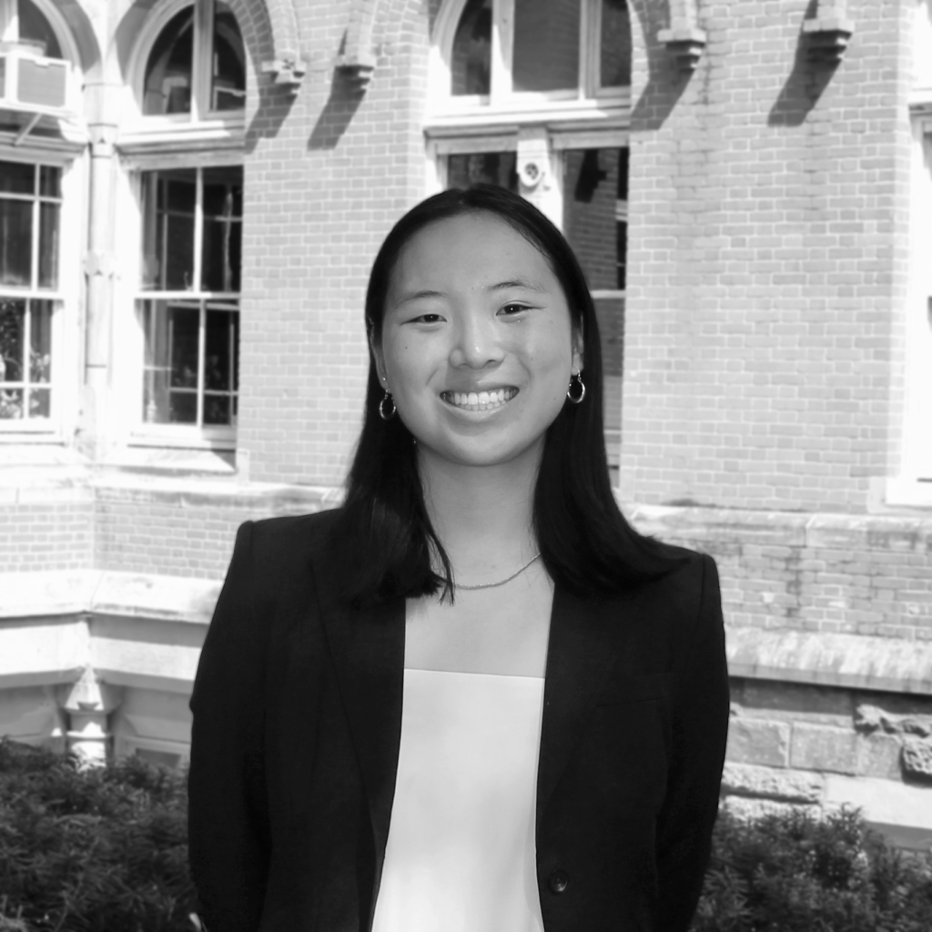 Alexa Nakanishi stands outside in front of brick building, black and white photo